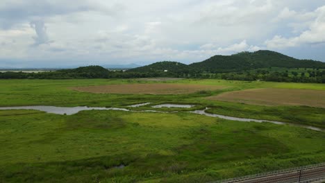 Aerial-footage-towards-hills-and-a-lake-revealing-a-railway,-farmlands,-waterways,-and-a-newly-harvested-farm