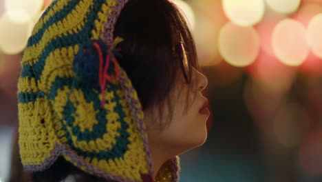 Closeup-of-girl-in-knitted-beanie-and-glasses-staring-up-to-bokeh-light-balls-at-fair