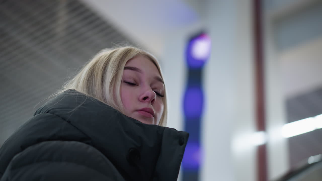 은 불빛이 박이는 흐릿한 배경과 함께 움직이는 에스컬레이터를 돌아보는 젊은 여성, 현대적인 도시 디자인과 움직임의 감각으로 매혹적인 관점