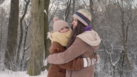 Front-View-Of-Mother-And-Daughter-In-Winter-Clothes-Hugging-In-A-Snowy-Forest