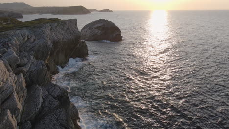 aerial view of sea waves breaking on rocky shore at sunset