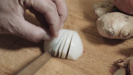 Imagen-De-La-Mano-Cortando-Cebolla-Blanca-En-Trozos-Pequeños-En-Una-Tabla-De-Madera-Junto-Al-Jengibre