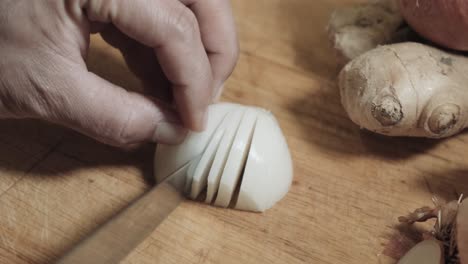 imagen de la mano cortando cebolla blanca en trozos pequeños en una tabla de madera junto al jengibre