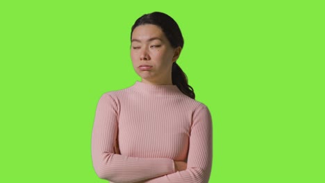 studio portrait of frustrated or angry woman standing against green screen