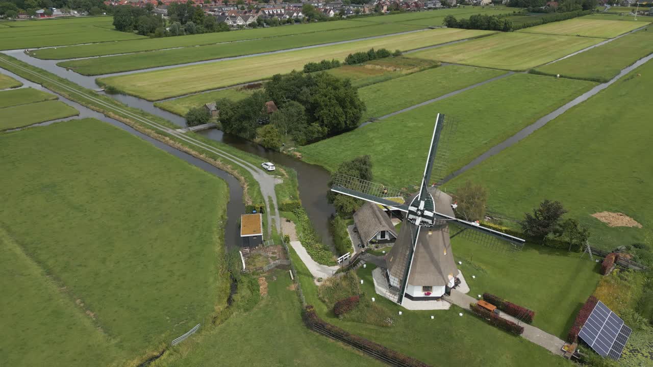 Aerial drone footage of a historic Dutch windmill in the middle of green farmland, surrounded by water canals near a village in the Netherlands