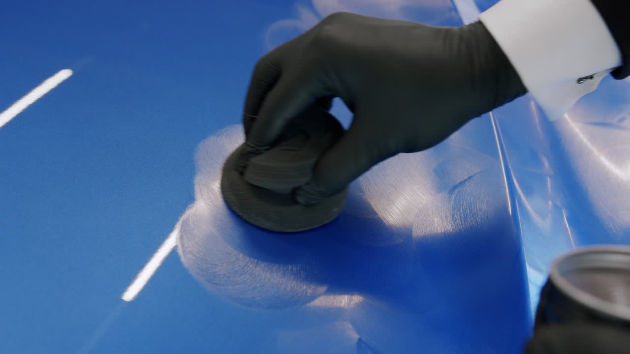 Close-up of a man in suit and gloves waxing the hood of a new car with a sponge