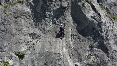 Climber-hanging-onto-a-mountain-as-camera-pulls-out-wide