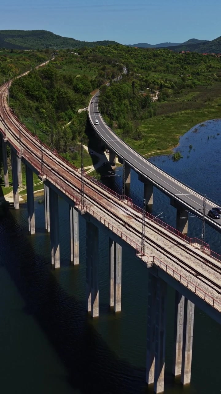 Vista panorámica de una vía férrea y una carretera junto a un río y colinas verdes