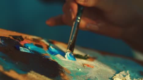 female artist mixing paints on palette with brush. woman hand holding paintbrush