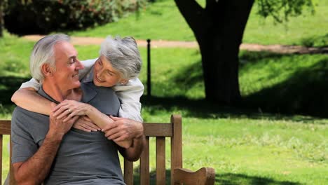 old woman hugging her husband sitting on a bench