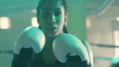 close up shot of a strong caucasian sportswoman training with coach, wearing boxing gloves and punching boxing paws