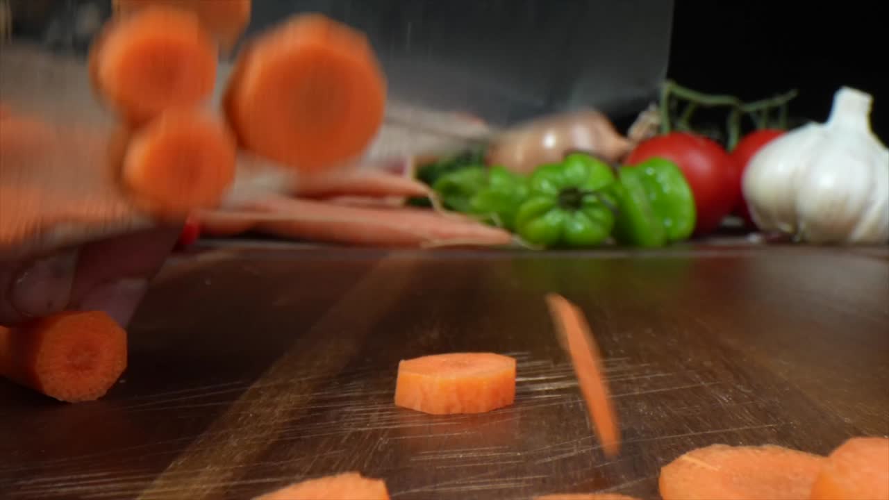 Close up of a carrot being quickly hand chopped in a kitchen on a wooden cutting board