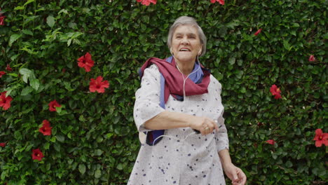 retrato de una anciana bailando brazos juguetones levantados disfrutando escuchando música en auriculares al aire libre fondo del jardín animada señora mayor