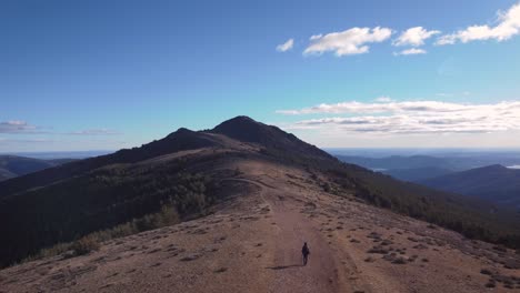 Aerial-shot-back-view-of-young-hiker-in-mountain-range-close-to-Madrid-during-afternoon-with-blue-sky-and-white-clouds