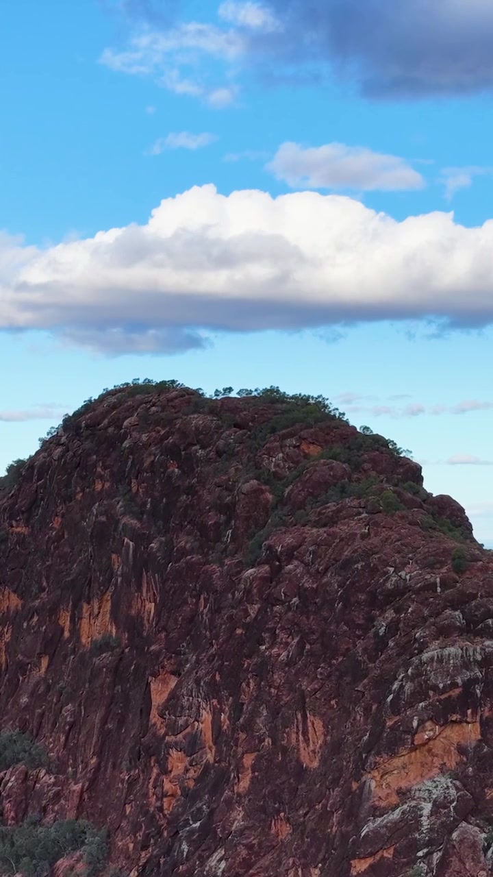 Picco montuoso di roccia rossa scosceso sotto un cielo blu con nuvole bianche.