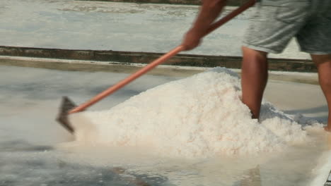 close-up of a man's arms pulling and gathering salt with a wooden shovel - rasoila