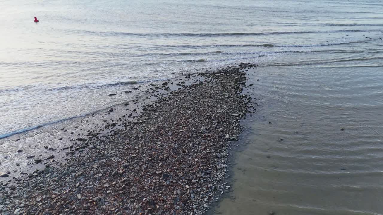 Two people in red walk on a tidal sandbar at low tide, captured by a drone in soft natural light, with gentle camera movement toward the sea