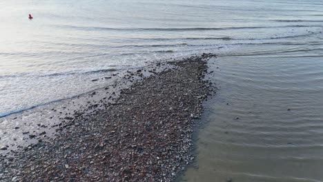 two people in red walk on a tidal sandbar at low tide, captured by a drone in soft natural light, with gentle camera movement toward the sea