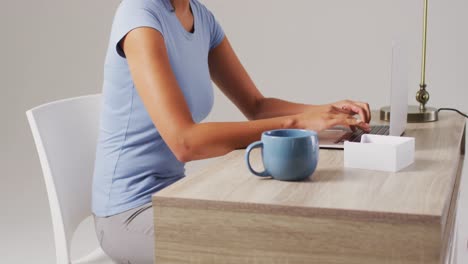 Video-of-midsection-of-biracial-woman-working-on-laptop-with-back-ache