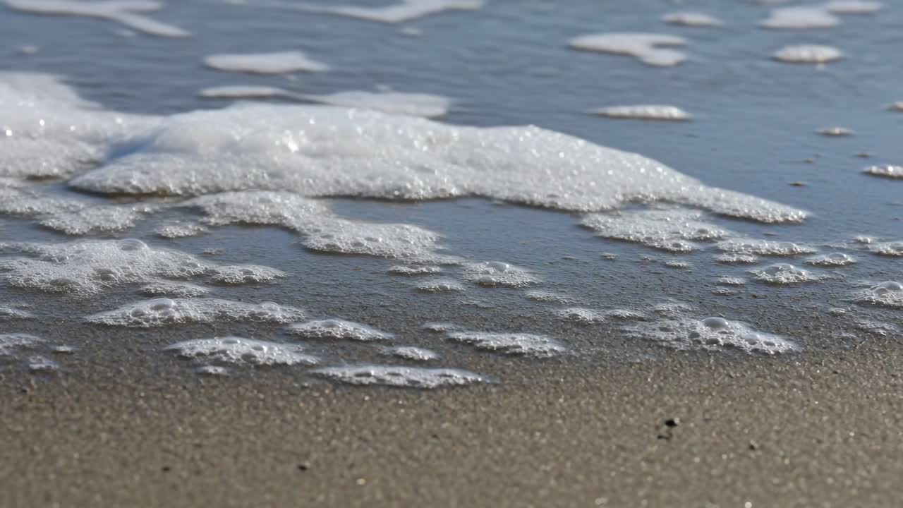 Rolling incoming surf coming from top of frame, spreading foamy water across wet sand and pebbles