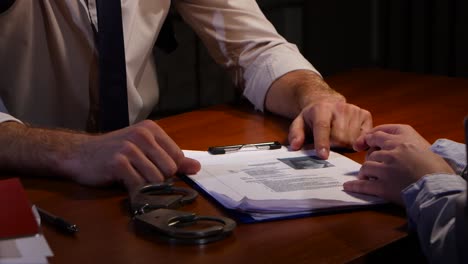 police man shows girl evidence against her closeup studio police man shows girl evidence against her in frame wooden table that displays the hands of suspected women and men policeman handcuffs and folder with documents and evidence closeup studio