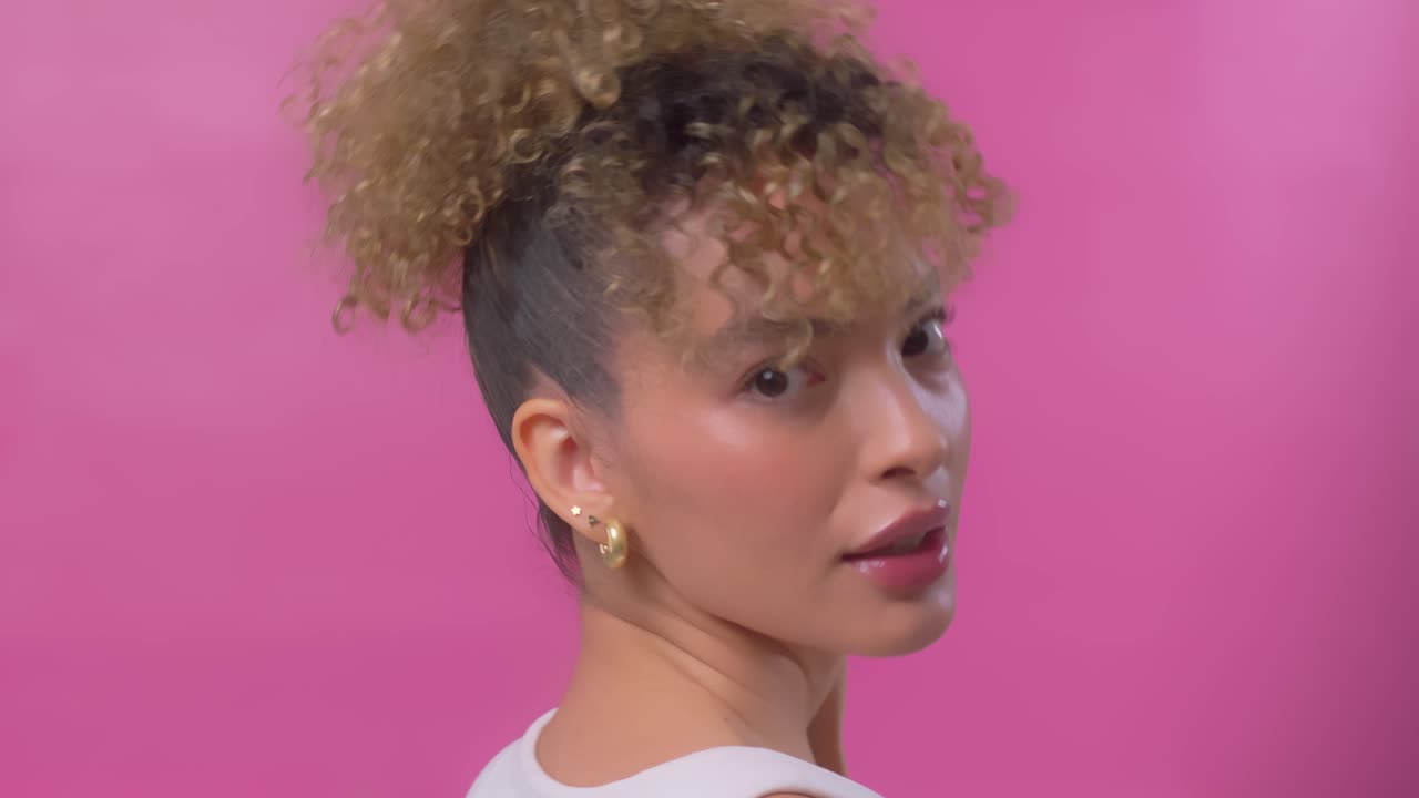 Young woman posing softly toward camera with glossy makeup and curly hair
