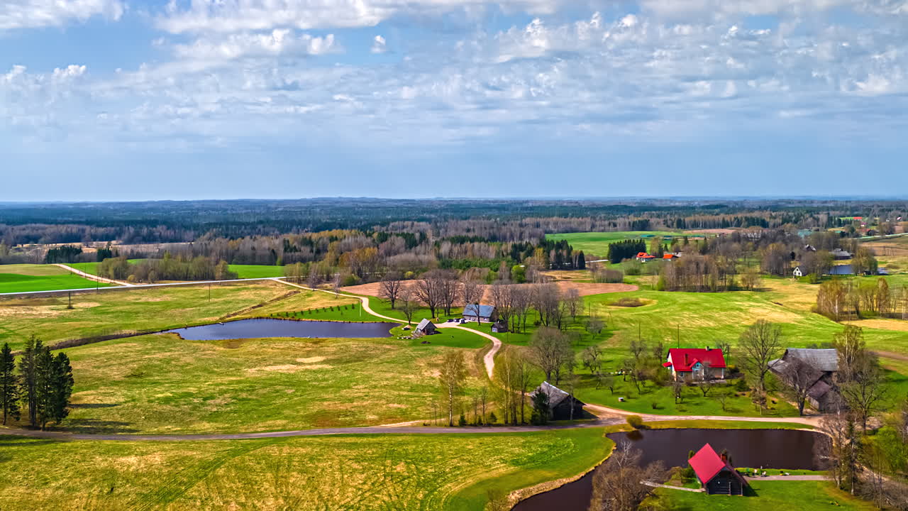 Hyperlapse of land featuring a few houses, small lakes, and surrounding forests, stretching to the horizon