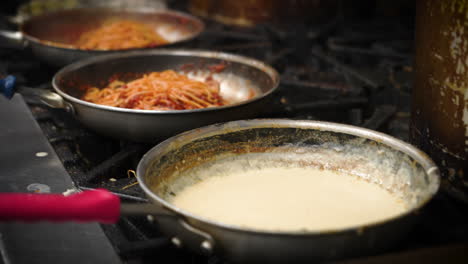 humeantes sartenes de salsa caliente alineadas en la estufa en la cocina de preparación del restaurante italiano llena de pedidos de pasta y salsa, cámara lenta 4k