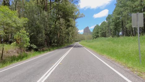 rear facing driving point of view pov of a deserted queensland country road with dramatic mount coonowrin framed by trees - ideal for interior car scene green screen replacement