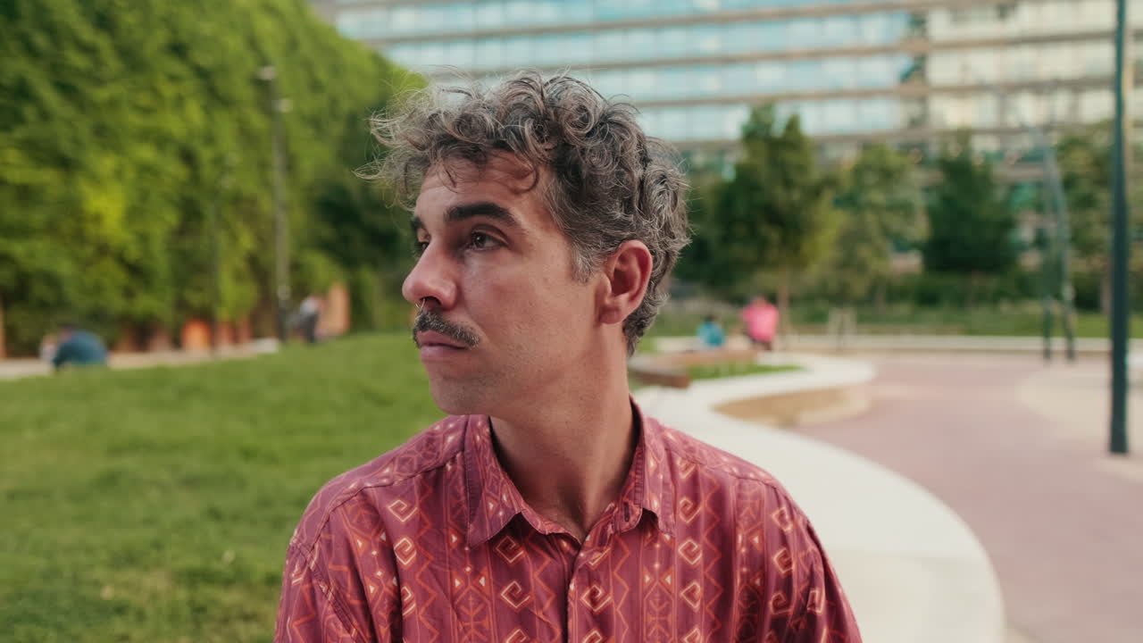Close-up de um homem com bigode olhando ao redor em um parque urbano