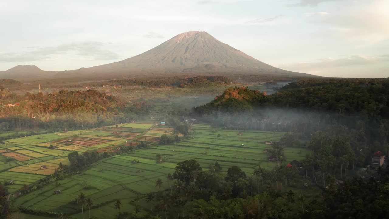 una vista espectacular del volcán mount agung con niebla matutina, luz del amanecer y campos de arroz verdes en bali, indonesia