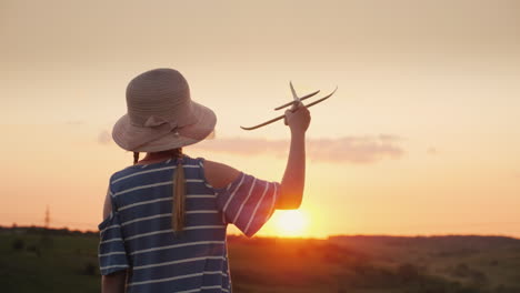 a girl with pigtails and a hat playing with a wooden airplane at sunset the dream of long-distance t