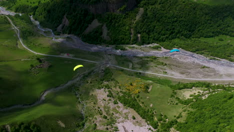 downward angle drone shot of a paraglider flying through a valley in gudauri georgia