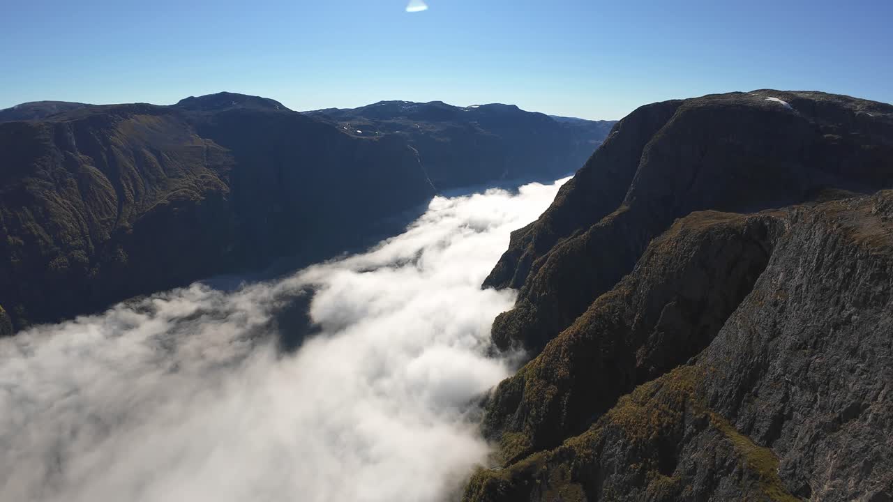 Aerial view over Naeroyfjord with cloud inversion far below, moving forward towards Gudvangen. Sunny day, grand UNESCO landscape