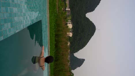 rear vertical shot of woman relaxing in outdoor pool looking at karst mountains in yangshuo, china