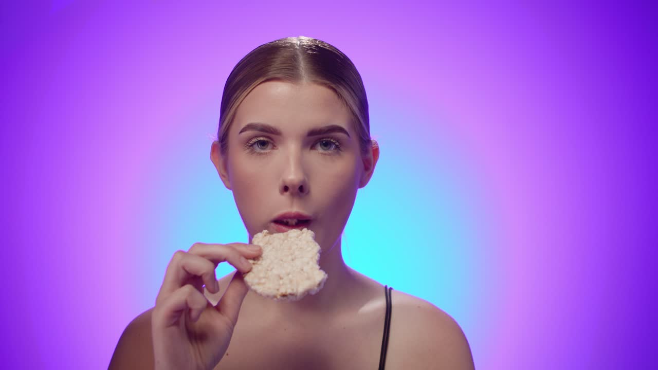Fittes Model isst Reiswaffel, um schlank zu bleiben, Studioaufnahme, isolierter violetter Hintergrund