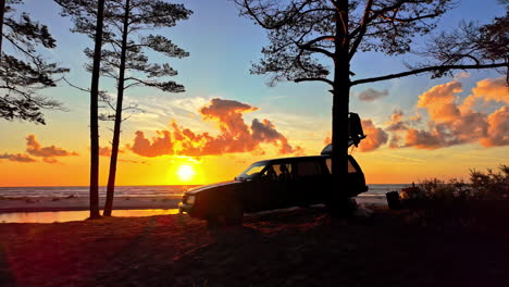 Slow-motion-landscape-scenic-view-of-car-vehicle-parked-on-remote-beach-seaside-surrounded-by-trees-with-sunset-nature-adventure-holidays-travel