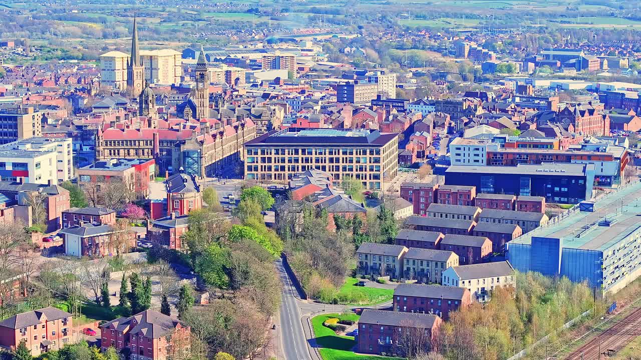 Aerial view of industrial suburb Wakefield, Yorkshire, Northern England, with busy roads, railway tracks, a historic cathedral landmark, and greenery stretching into the distance.