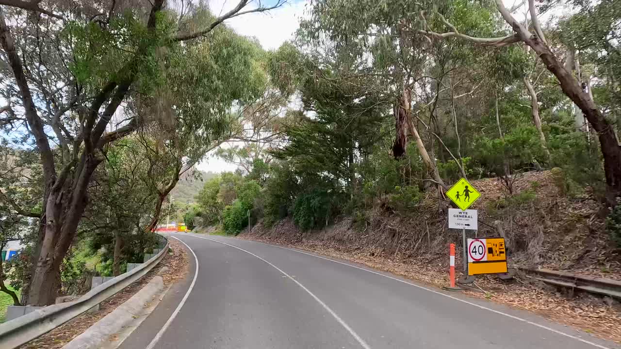 A drive through lush greenery on Great Ocean Road, ending at a roadwork site under bright daylight