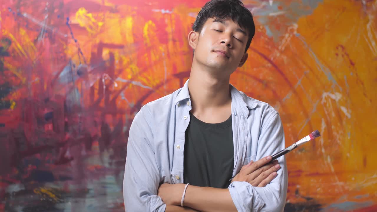 Male Artist With Paint, Crosses Arms While Holding Brush, Looks At The Camera With A Smile
