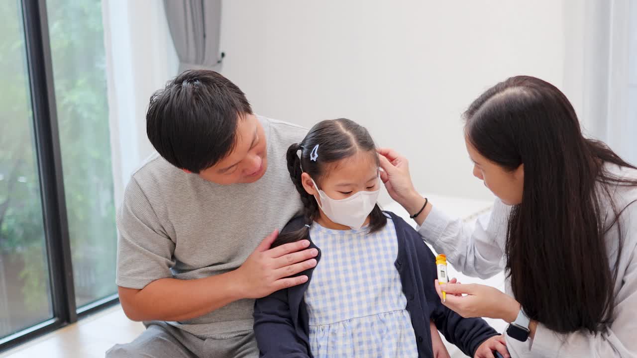 Mother and father comfort sick daughter, remove mask, and check temperature in bright bedroom