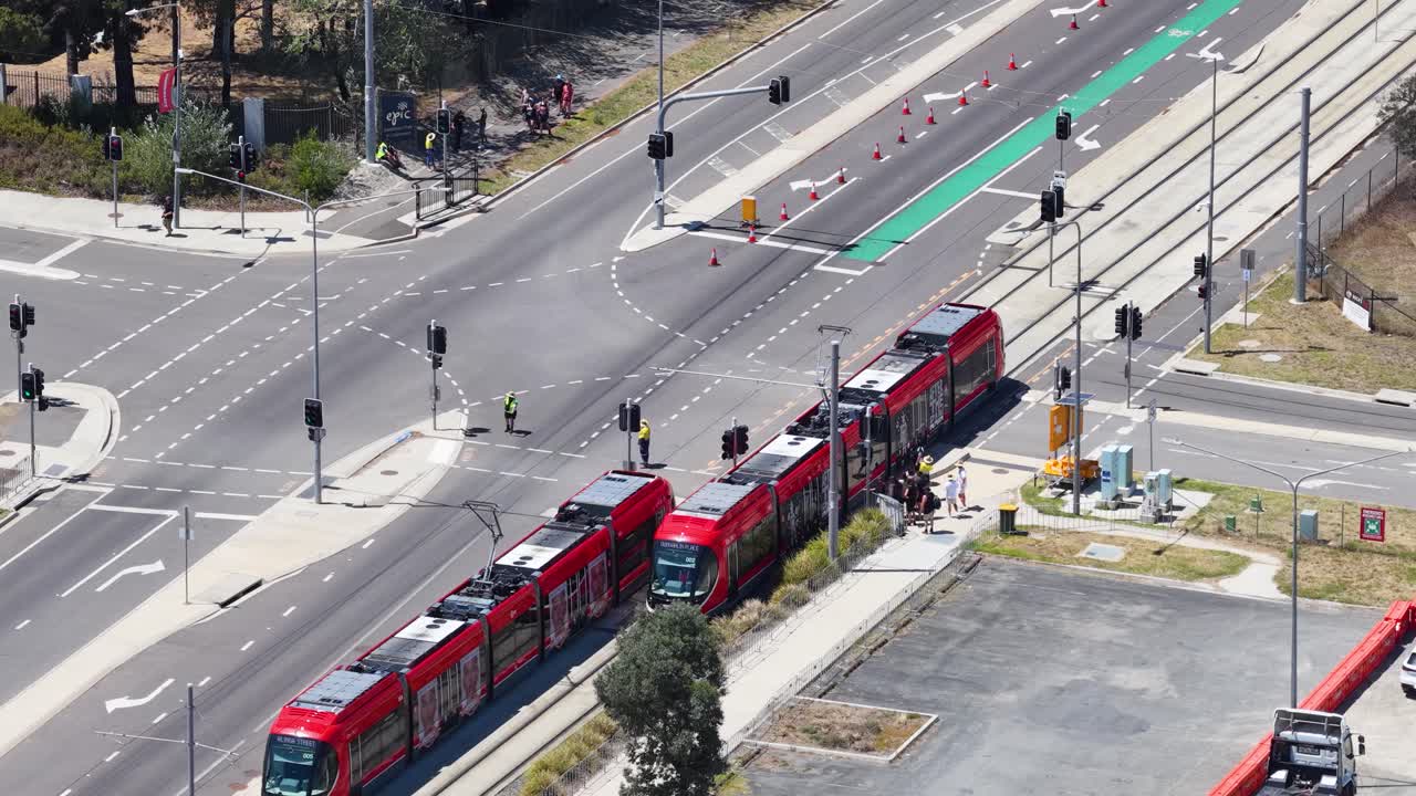 Eine Drohnenaufnahme aus hohem Winkel fängt rote Stadtbahnen ein, die sich durch eine australische Vorortkreuzung bewegen