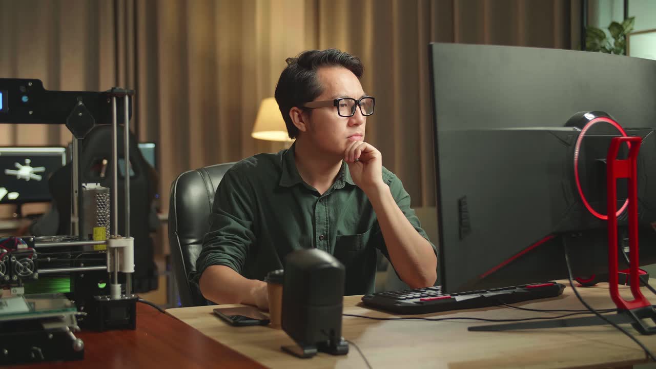 Asian Man Thinking While Works On Personal Computer And 3D Printer In Home Office, He Works At Night