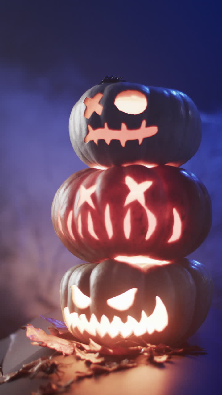 Vertical video of halloween carved pumpkins and smoke with copy space on blue background
