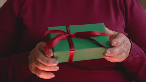 close up view of a woman's hands holding christmas gift from a box sitting on the sofa