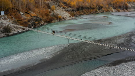 Zwei-Einheimische-Frauen-überqueren-Vorsichtig-Die-Hussaini-Hängebrücke-über-Den-Hunza-Fluss-In-Pakistan