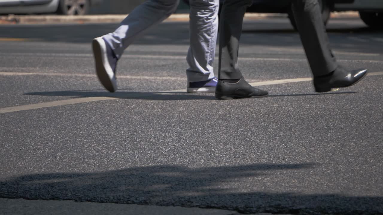 Low Angle View Of Three People's Legs Crossing The Road