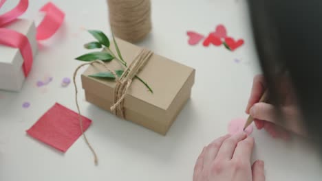 woman signs small note on paper circle to tie to present box