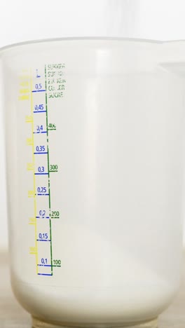close-up vertical shot of sugar being poured into a measuring cup during tiramisu preparation.
