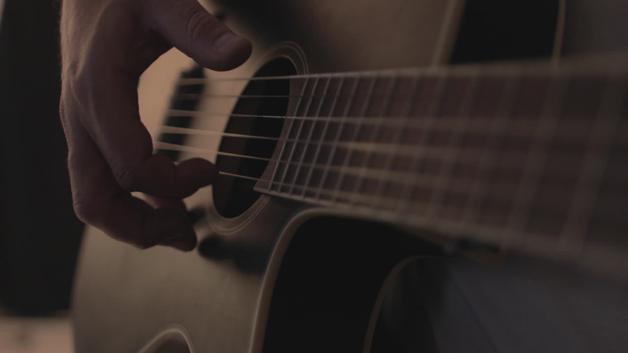 Mężczyzna grający na gitarze akustycznej na czarnym tle z miękkim, ciepłym światłem